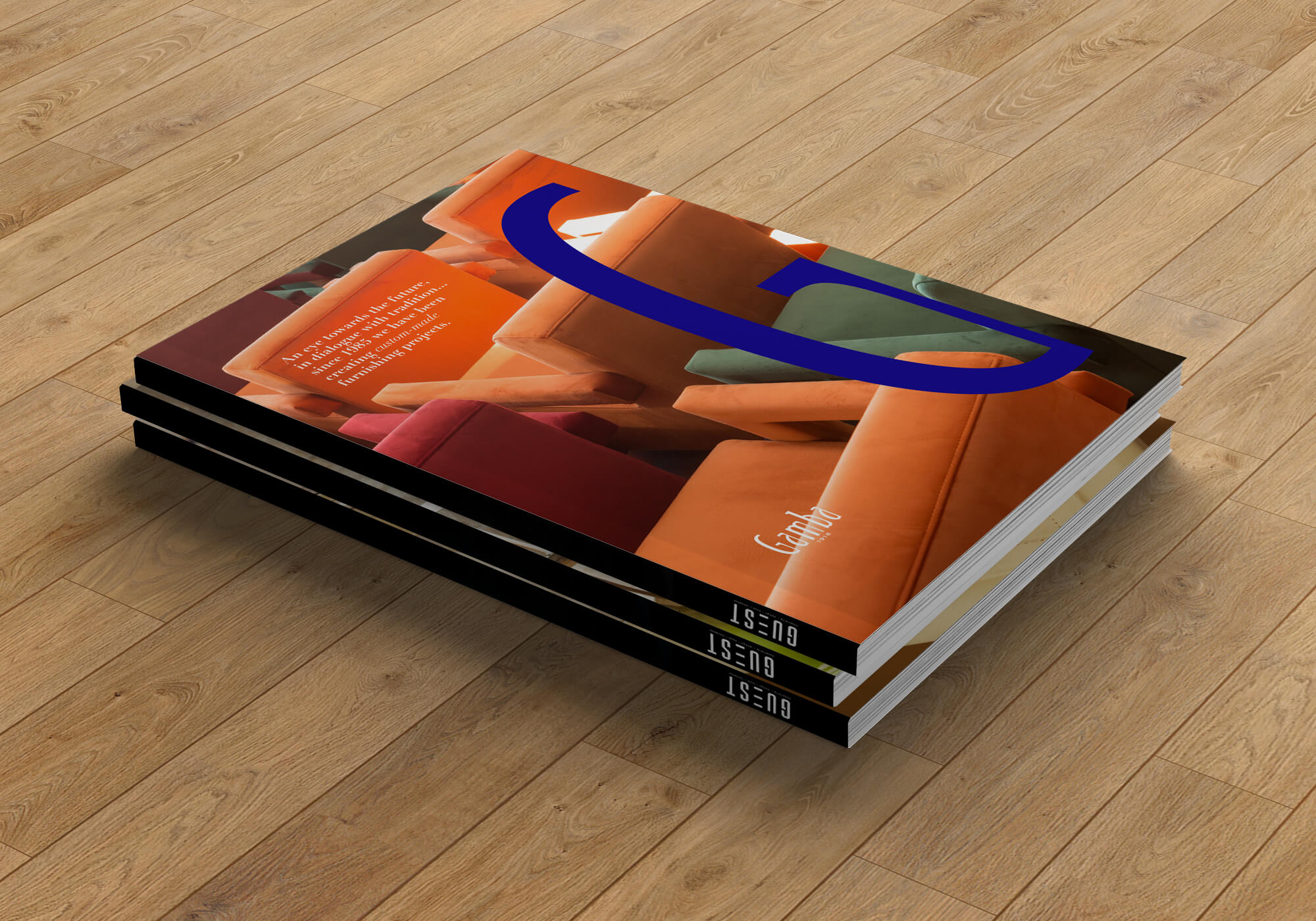 Stack of three magazines on a wooden floor with a cover showing colorful upholstered chairs in orange, green, and red, large blue text overlay, and smaller white text reading an introduction about custom-made furnishing projects.