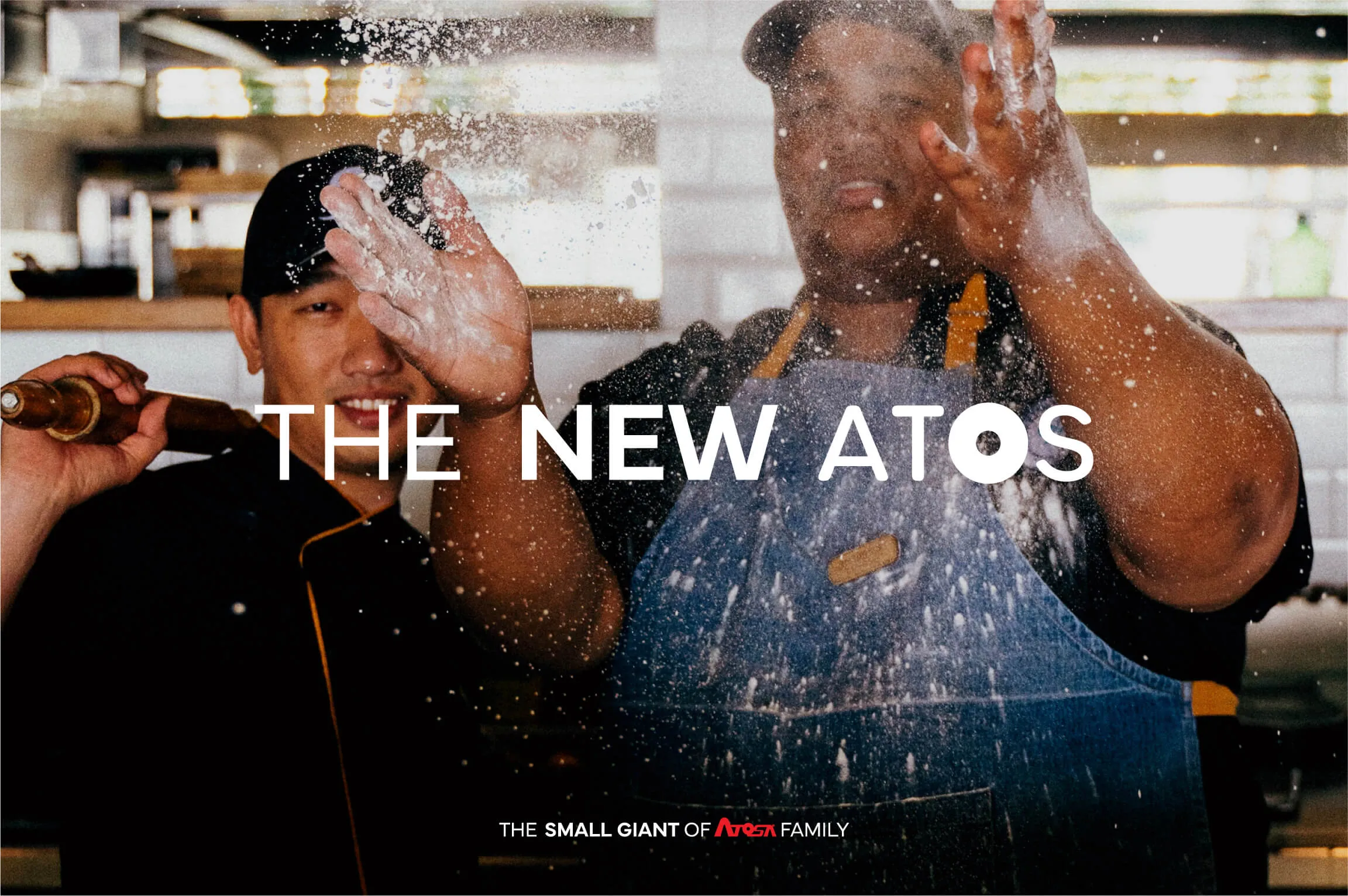 Two chefs in a kitchen, one tossing flour in the air with hands covered in flour, the other holding a rolling pin, both smiling with text overlay: 'THE NEW ATOS' and smaller text 'THE SMALL GIANT OF ATOSA FAMILY'.