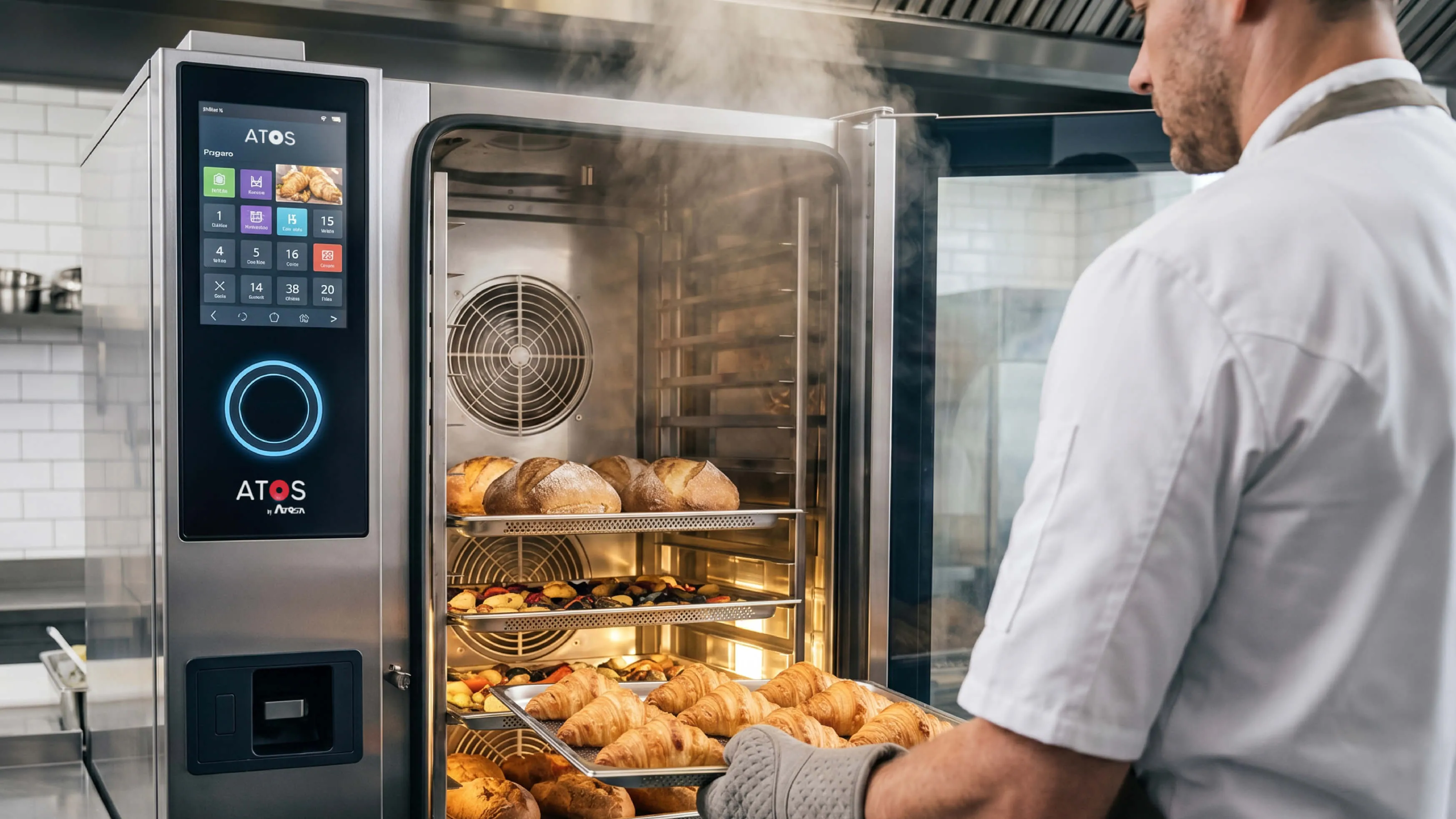 A baker in a white shirt places a tray of freshly baked croissants into a modern stainless steel commercial oven with steam rising inside and other baked goods on racks.