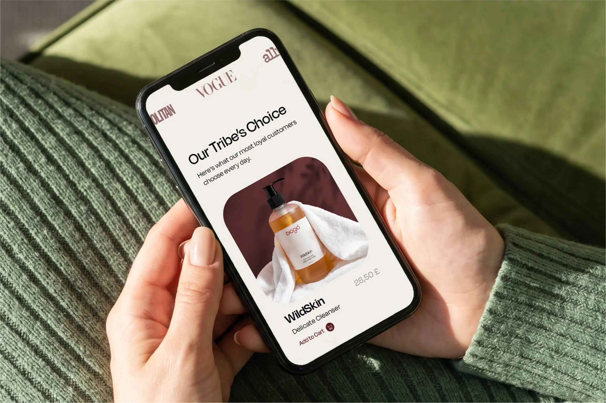 Hands holding a smartphone displaying a skincare product page for WildSkin Delicate Cleanser priced at 28.50 pounds, with the header Our Tribe's Choice and an image of the product bottle wrapped in a white towel.