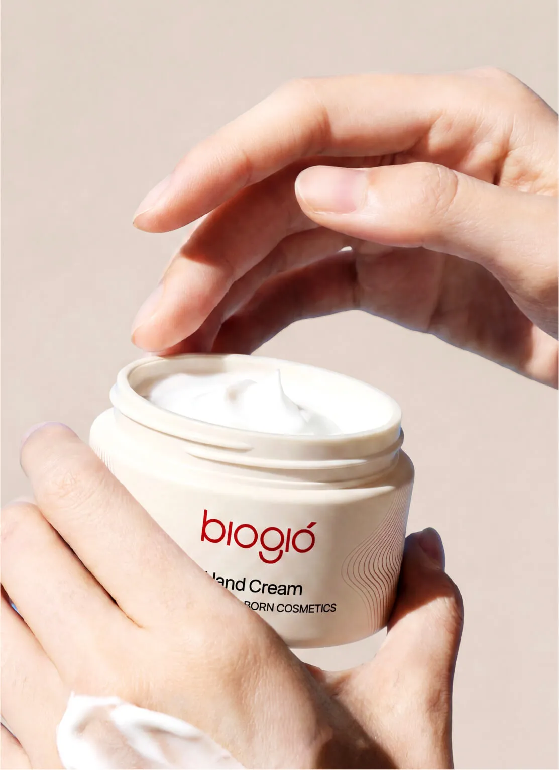 Hands holding an open jar of Bioglo hand cream with a scoop of white cream inside.