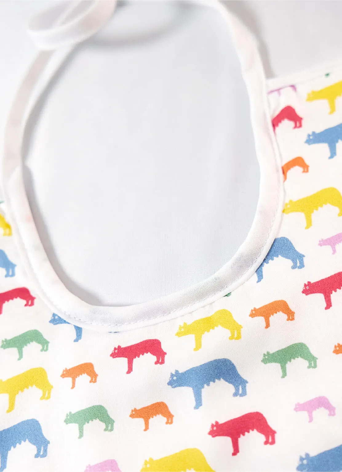 White baby bib with a colorful pattern of wolves in red, yellow, blue, green, orange, and pink scattered across the fabric.