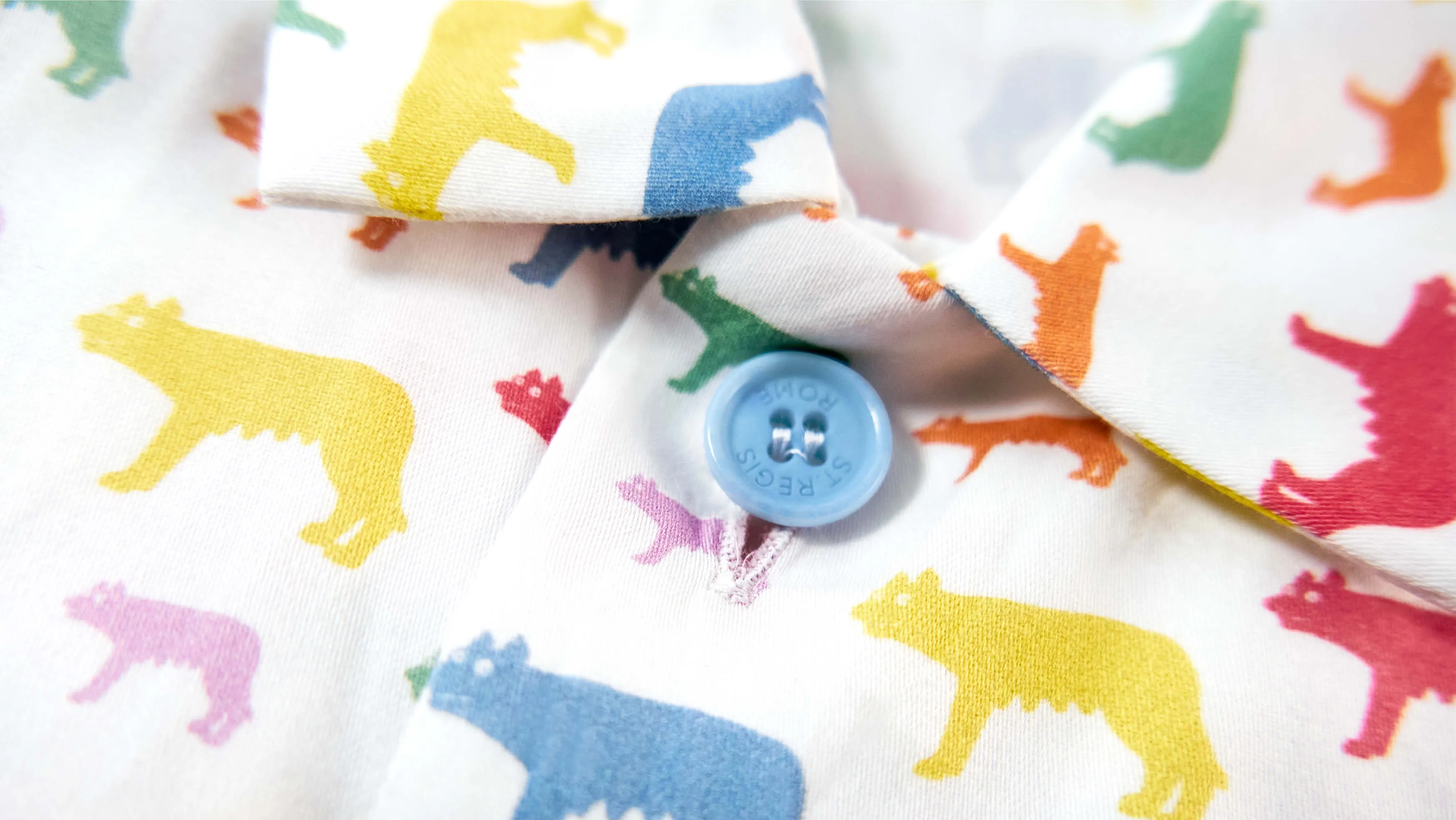 Close-up of white fabric with colorful wolf silhouettes in yellow, blue, purple, green, orange, and red, and a light blue button with the word ST REGIS embossed.