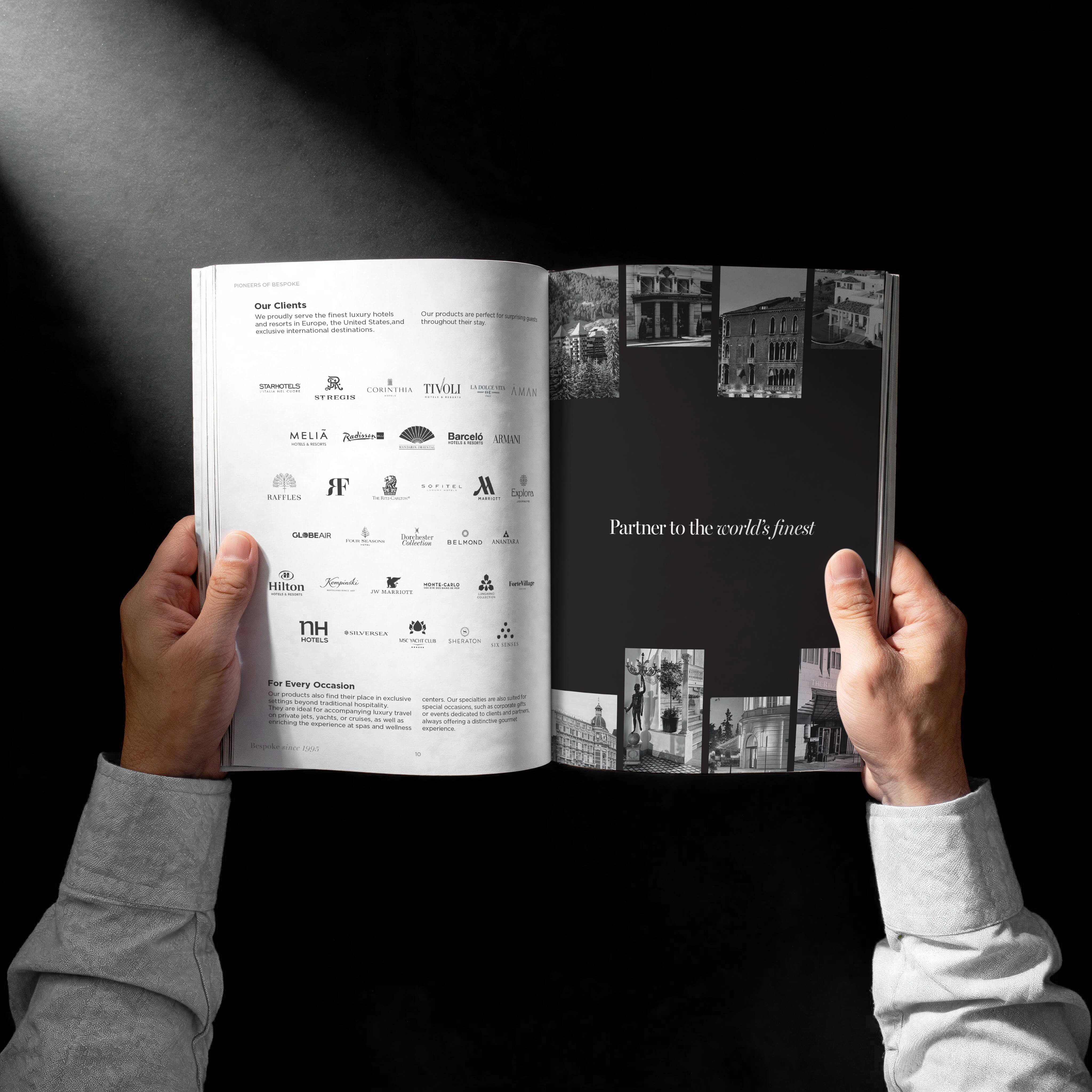 Person holding open a magazine with two pages visible: the left page lists luxury hotel client logos and brief text about serving luxury hotels and resorts in Europe, the US, and exclusive destinations; the right page has a black background with white text reading 'Partner to the world's finest' surrounded by small black and white images of elegant buildings and interiors.