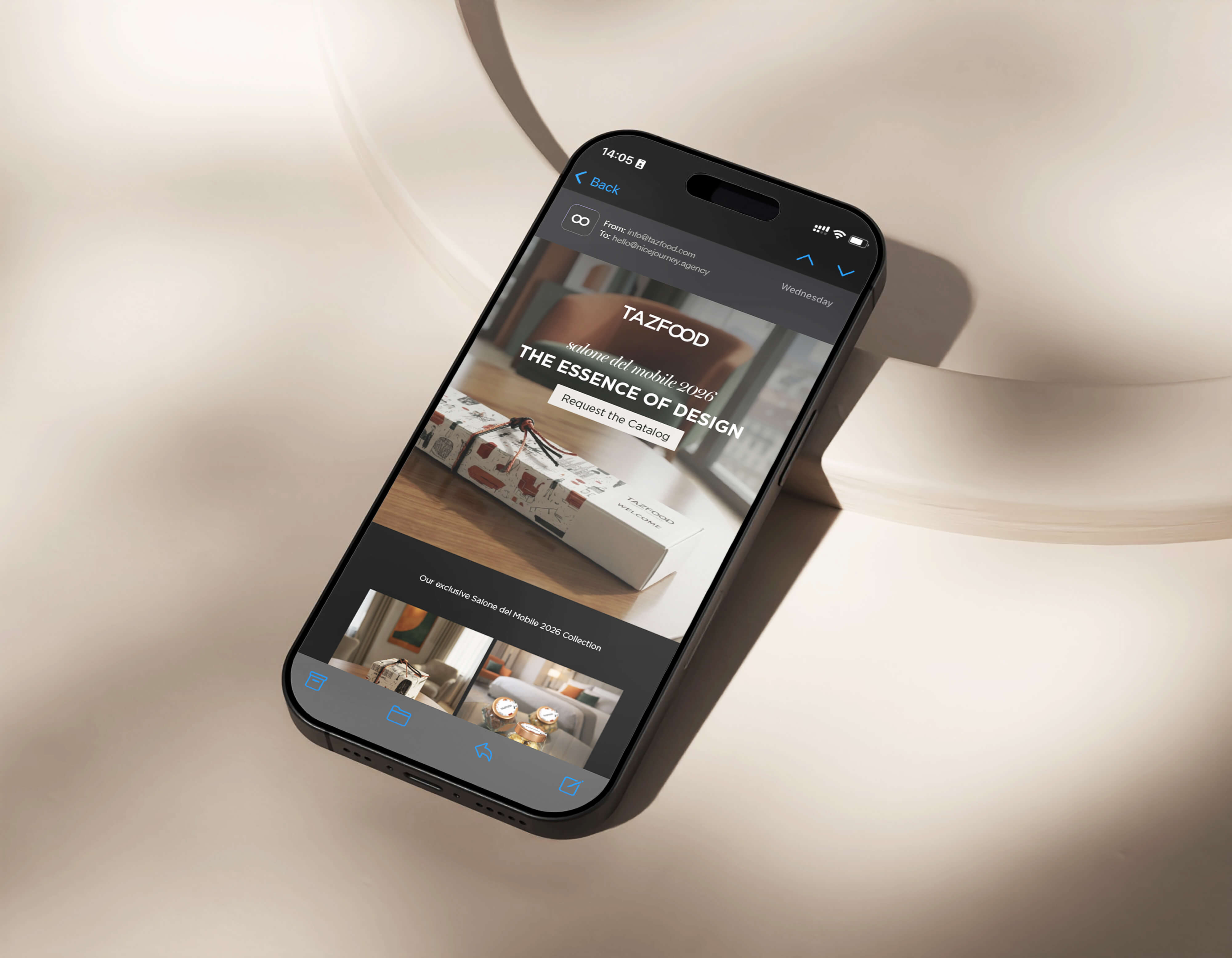Smartphone displaying an email from TAZFOOD about Salone del Mobile 2026 with the headline 'The Essence of Design' and a button to request the catalog, resting on a beige surface.
