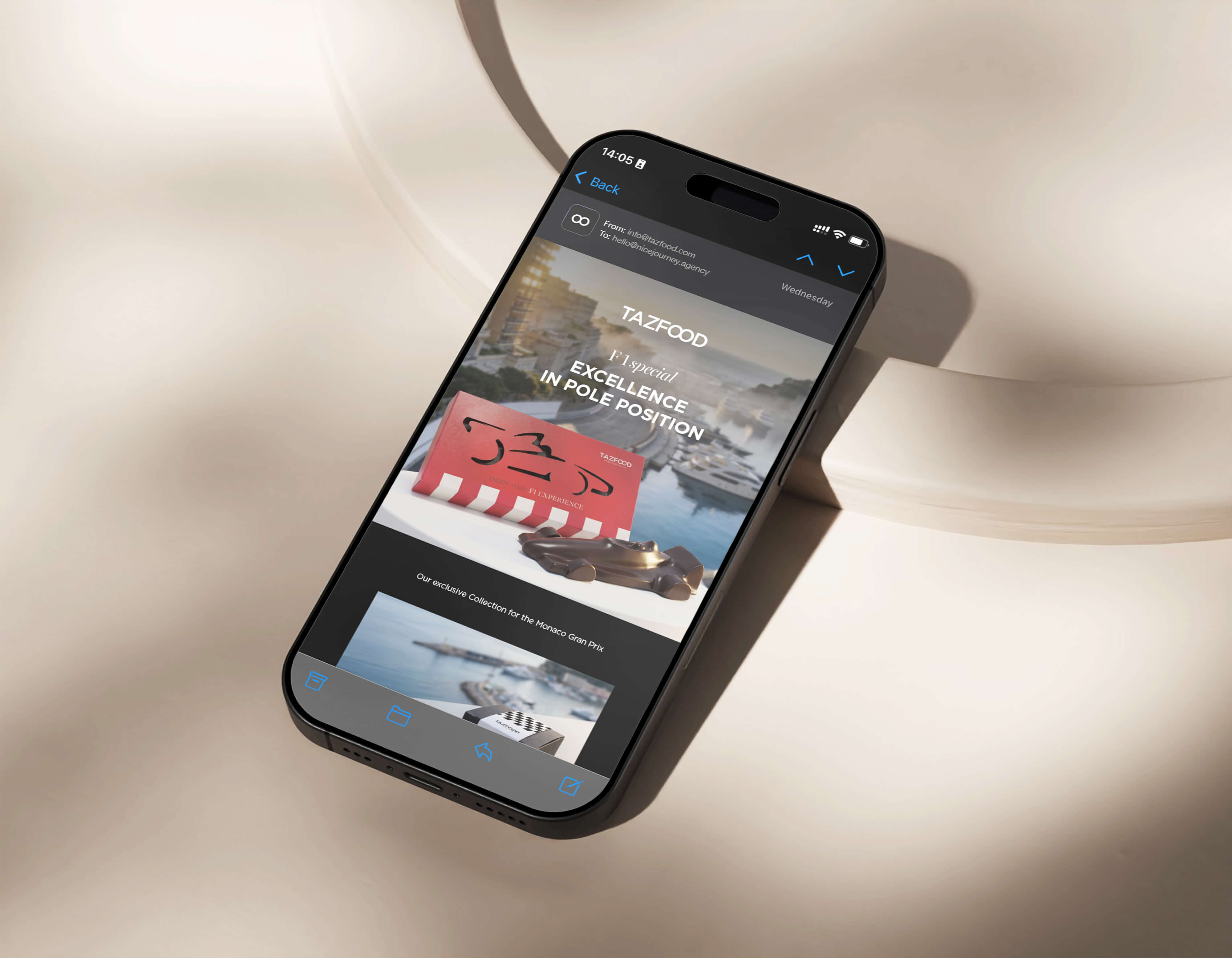 Smartphone lying on a beige surface displaying an email from TAZFOOD with the header 'EXCELLENCE IN POLE POSITION' and images featuring a red branded box and miniature race car model against a marina backdrop.