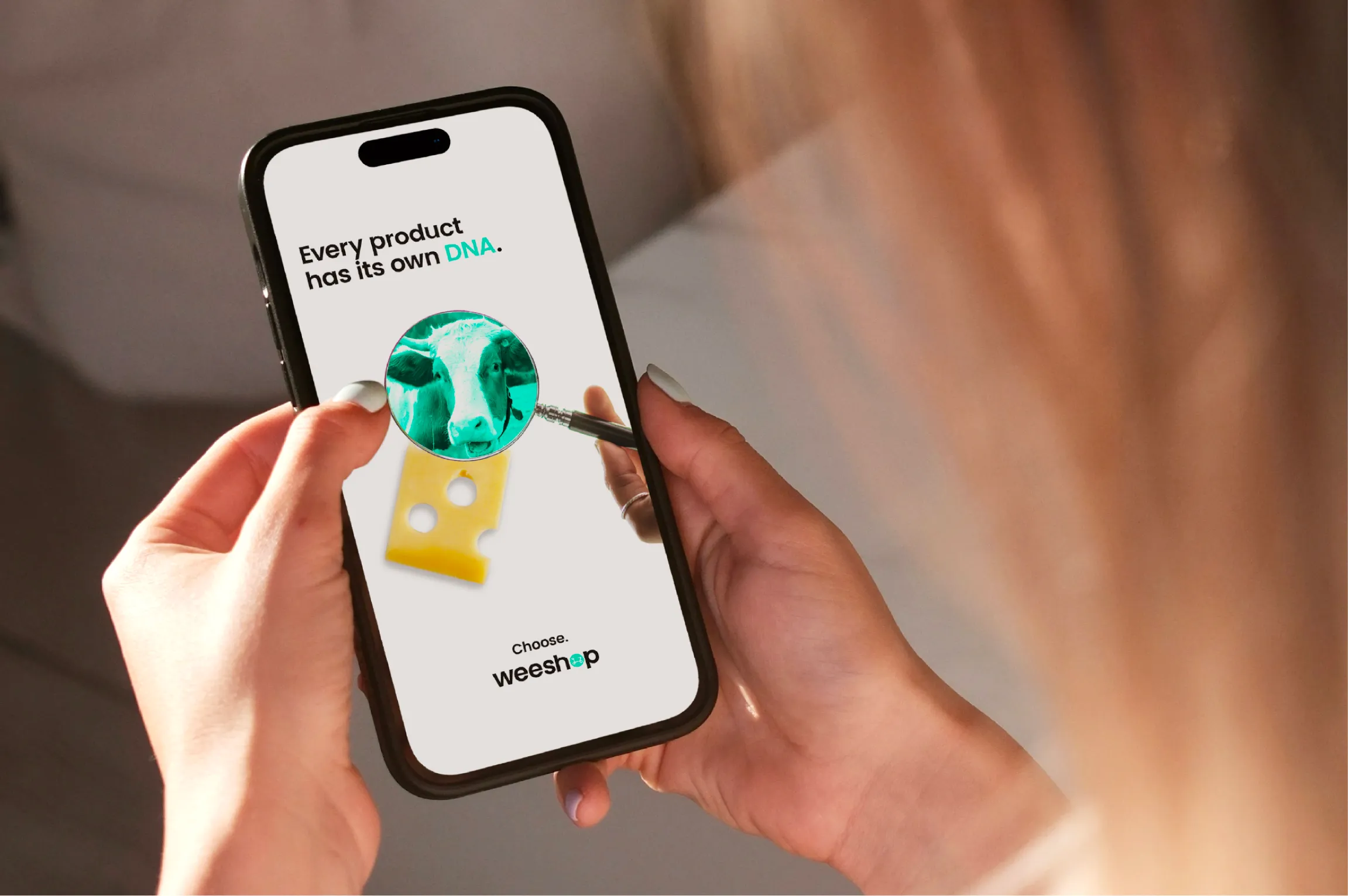 Person holding smartphone displaying an ad that says 'Every product has its own DNA' with image of cheese and a magnifying glass revealing a cow's face inside it, and text 'Choose weeshop' below.